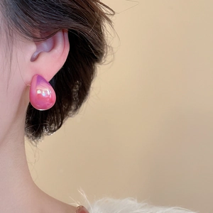 Close-up of iridescent teardrop stud earrings with pink gradient on model's ear