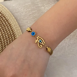 Detail of gold evil eye bracelet with Horus eye charm and blue beads on a wrist