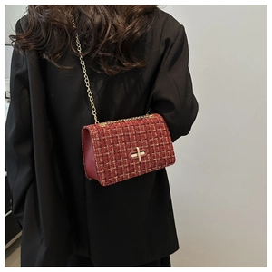 Model wearing red tweed shoulder bag with gold chain and black blazer in a minimalist indoor setting