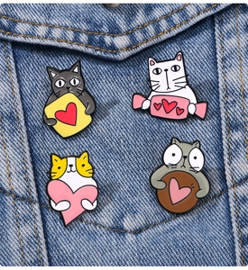 Detail of four cute cartoon cat enamel pins pinned on a blue denim jacket pocket