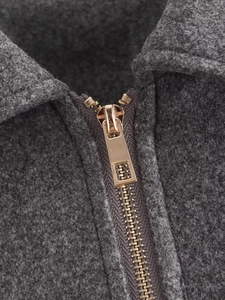 Detailed macro view of dark grey wool jacket featuring a premium golden metal zipper finish