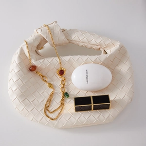 Borsa a mano intrecciata color crema con collana dorata e accessori di bellezza di lusso