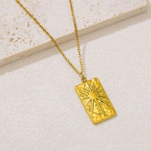 Close-up of golden rectangular sunburst pendant on a fine chain with relief detail
