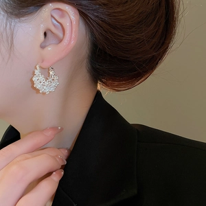 Close-up of pearl hollow flower basket U-shaped earrings on a model with elegant black suit