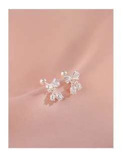 Detailed macro view of silver bow and lily of the valley earrings on pink satin