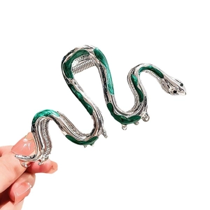 Silver snake-shaped hair claw clip with green enamel finish held in a hand close-up view