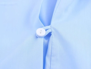 Gros plan sur un bouton blanc et la texture du tissu d'une chemise bleu clair