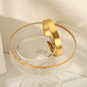 Polished gold and silver stainless steel bangles set on a glass edge in warm lighting