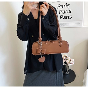 Close-up of brown faux leather baguette bag with bow and heart pendant detail