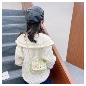 Detail of green tweed girls crossbody bag with pearl handle and floral bow decoration