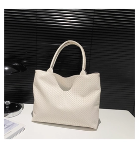 Close-up of cream woven leather tote bag with Intrecciato texture on white desk