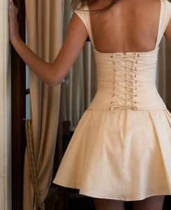 Detail view of beige mini dress featuring lace-up back design and pleated waist for women