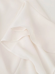 Detailed close-up of ruffle trim and soft chiffon fabric texture on beige top