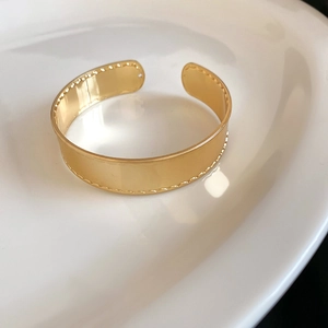 Nahaufnahme eines polierten goldenen Armreifs mit elegantem, gewelltem Rand-Design-Detail