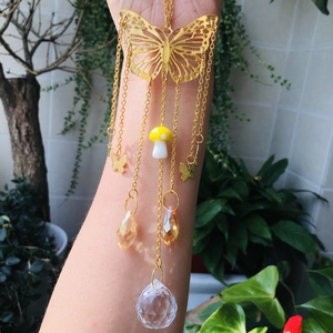 Detail of golden butterfly suncatcher with crystal prisms and mushroom charm outdoors