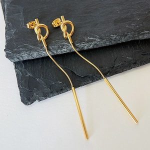 Close-up of gold knot tassel earrings in 18k plated steel on black slate surface