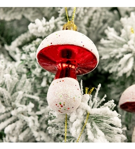 Detail of red and white mushroom ornament with glitter hanging on a snowy Christmas tree