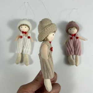 Detailed view of hand holding small knitted doll ornaments with red bows for Christmas tree