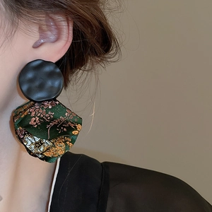 Detail of vintage earrings with black ripple metal and green floral embroidery