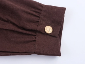 Detail of dark brown linen blazer sleeve with gathered cuffs and gold textured button
