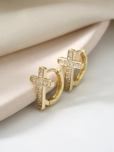 Macro shot of gold cross hoop earrings with white zircon pavé on beige silk fabric