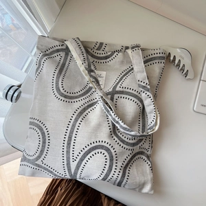 Detail of grey canvas tote bag featuring abstract black wave patterns and wide straps