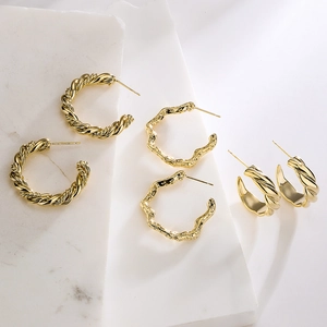Three pairs of elegant gold-plated twisted rope C-shaped hoop earrings on white marble