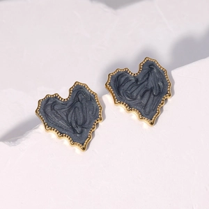 Macro shot of heart-shaped gold-rimmed stud earrings with dark grey swirl texture