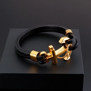 Close-up of black leather wrap bracelet with gold anchor and cross clasp on black display box