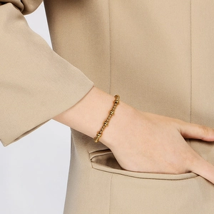 Détail d'un bracelet en perles d'acier doré 18 carats porté au poignet aux tons chauds