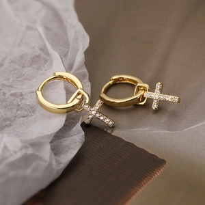 Gold-plated cross drop earrings with shimmering zircon stones on a minimalist background