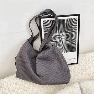 Close-up of pleated dark grey hobo bag with adjustable strap on white faux fur rug