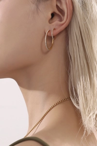Detail of elegant gold hoop earrings with pavé zircon worn by a model in soft lighting