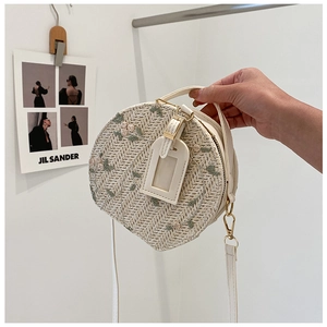 Detailed close-up of a round straw bag with floral embroidery and white leather handle