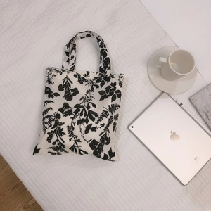 Minimalist white canvas tote bag featuring black floral prints with daily life accessories