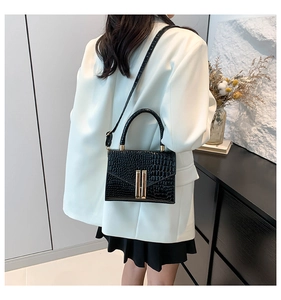 Detailed view of black crocodile pattern handbag with gold clasp on a white suit model