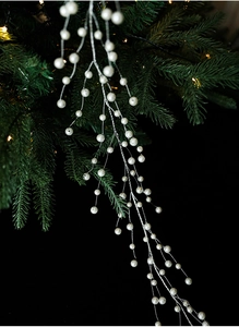 Detail of white pearls on silver wire hanging on green Christmas tree branches