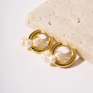 Detailed close-up of golden hoop earrings with clustered white pearls on stone surface