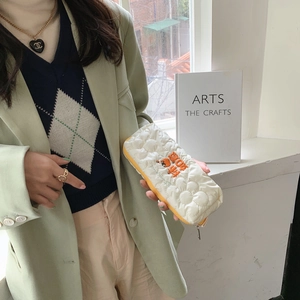Close-up of quilted white pencil case with orange embroidery and yellow zipper piping