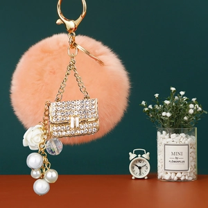 Detail of coral faux fur pompom keychain with a rhinestone mini bag and pearl charms