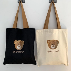 Detail of canvas tote bag featuring embroidered bear and Japanese text with brown handles