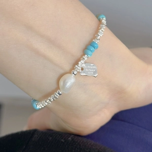 Macro view of a 925 silver anklet with blue beads, fresh water pearl, and metal tag