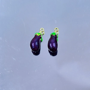 Detailed view of two eggplant-shaped enamel charms with purple finish and green leaves