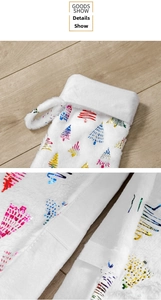 Detail of white plush Christmas stocking featuring colorful foil tree prints and velcro closure