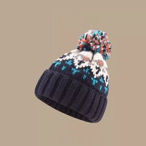 Detail of blue knit beanie featuring colorful pom-poms and vibrant geometric patterns