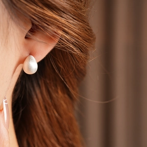 Close-up of minimalist brushed silver water drop stud earring on a model ear
