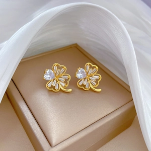 Macro shot of gold clover earrings with micro-inlaid white zircon on silk fabric