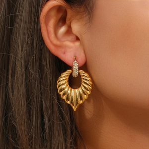 Close-up of gold seashell textured drop earrings with sparkling rhinestone studs