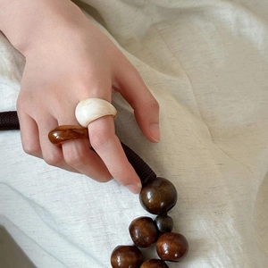 Close-up of marble pattern resin rings in cream and amber on hand with wooden beads