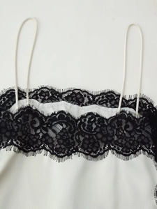 Detail eines weißen Satintops mit schwarzer Wimpernspitze und feiner Seidentextur